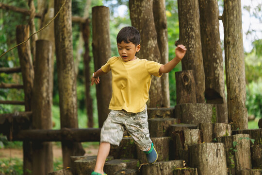 Young child navigating a natural wooden obstacle playground in a forest, balancing across log steps during active outdoor play, exploration and nature-based recreation.