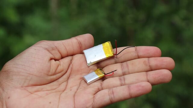 Holding two small lithium polymer battery cells of different sizes with wires on natural light close up view