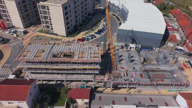Barcelos, Braga, Portugal - 18 September 2026: Aerial view of a construction site featuring a tall yellow crane, concrete foundations, and rebar in an urban area.