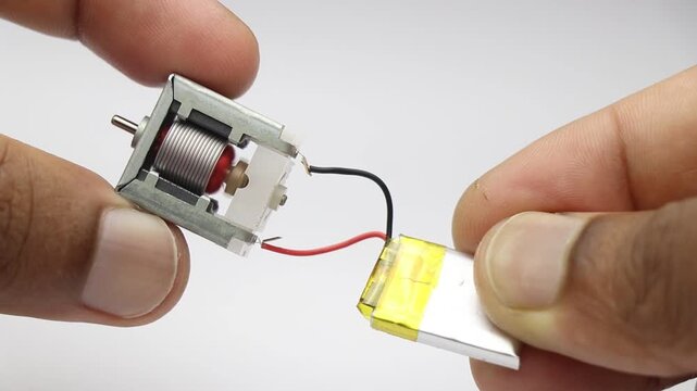 Testing small electric dc motor with mini lithium polymer battery direct wire connection with close up of hand holding components