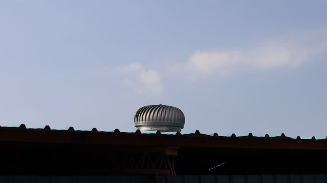 Metal roof turbine ventilator spinning on rooftop against clear blue sky close up shot