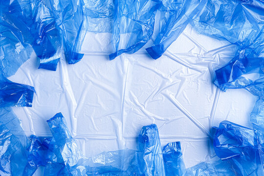 Single-use plastic shopping bags on wrinkled light blue synthetic background, frame with empty space. Plastic texture as concept of everyday consumer packaging and use of disposable plastic products.