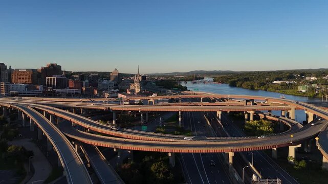 Complex highway interchange and curving overpasses spanning above the Hudson River and downtown Albany New York under a golden sunset sky 4k aerial drone video