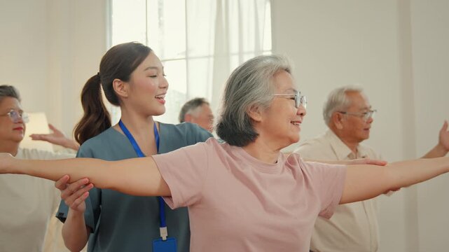 Caregiver senior wellness nursing home exercise group with older adult stretching arm in gentle indoor fitness class for mobility health balance support
