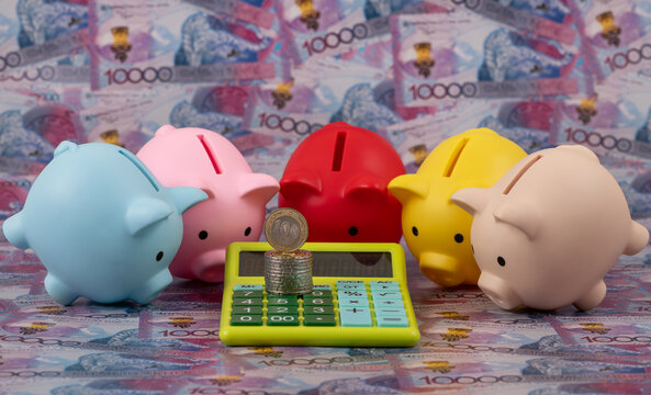Piggy banks and a calculator against a background of 10000 Kazakhstani tenge banknotes.