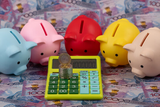 Piggy banks and a calculator against a background of 10000 Kazakhstani tenge banknotes.