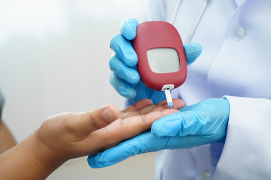 Asian doctor using digital glucose meter for check sample blood sugar level to treatment diabetes.