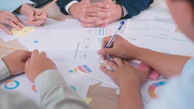 Business team holding pens write notes, sign documents, and analyze financial data during a strategic meeting in a corporate office.