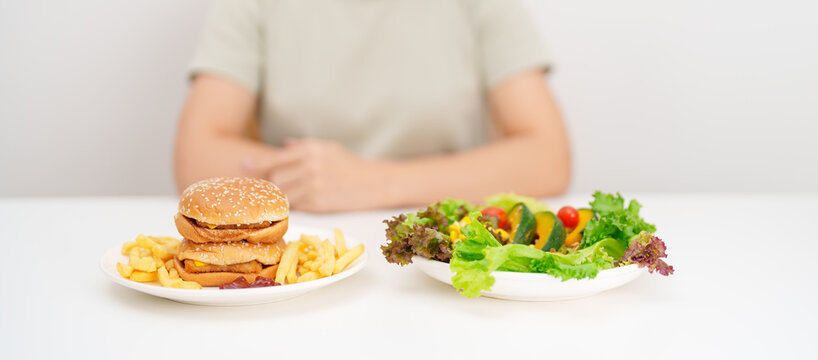 happy woman with Healthy and Unhealthy Food Choice. Comparison of Calories and Nutrition of vegetables Salad plate and Hamburger. diet planning, weight loss management, junk food and habit lifestyle