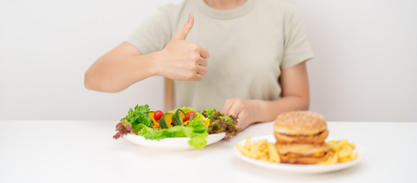 happy woman choose vegetables Salad and thumbs up gesture. Healthy and Unhealthy Food Choice, Calories and Nutrition of vegetables and Hamburger. dieting, weight loss control, junk food and lifestyle