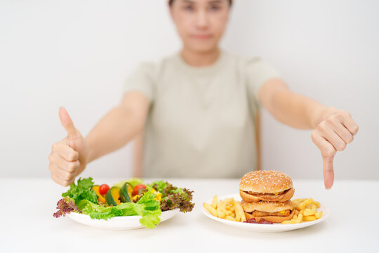 Comparison of woman with vegetables Salad and thumbs up and Hamburger show thumbs down. Healthy and Unhealthy Food Choice. dieting management, weight loss control, junk food and habit lifestyle