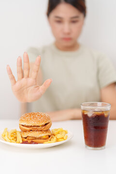 Unhappy woman showing Rejecting and refusing with Juicy beef burger, potato chips and carbonated Soft drinks. Unhealthy, High calorie, Fast food craving, Obesity, diet, weight loss and junk food