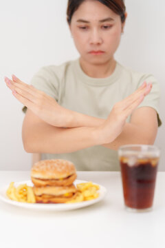 Unhappy woman showing Rejecting and refusing with Juicy beef burger, potato chips and carbonated Soft drinks. Unhealthy, High calorie, Fast food craving, Obesity, diet, weight loss and junk food