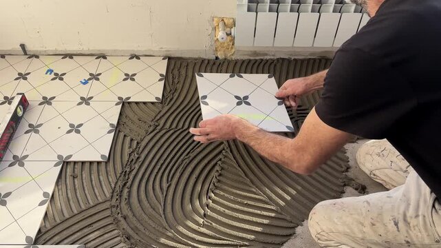 Professional tile installer spreading tile adhesive with a notched trowel on the floor before laying ceramic tiles during home renovation