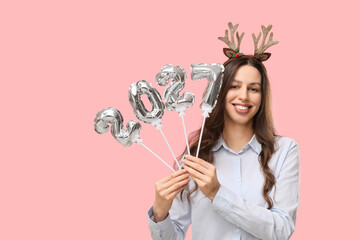 New year celebration and holiday planning, happy young woman holding silver 2027 balloons with reindeer antlers on a pink background © Pixel-Shot