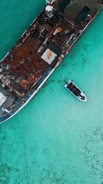 Drone view of motorboat exploring large abandoned vessel wreck in tropical turquoise water. Concept of diving tour, maritime adventure, sea discovery, and vacation excursion.Vertical video