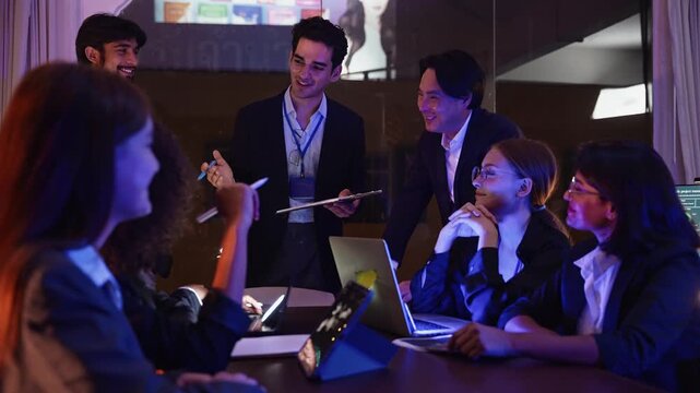Business team gathers in a meeting room for a late night project review, sharing ideas and collaborating closely with laptops and notes to solve complex problems together.