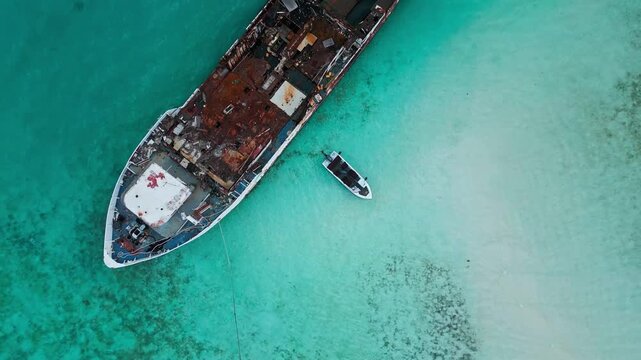 High angle drone perspective showing size contrast between modern speed boat and decaying abandoned ship wreck. Concept of scale, history vs present, and human intervention.