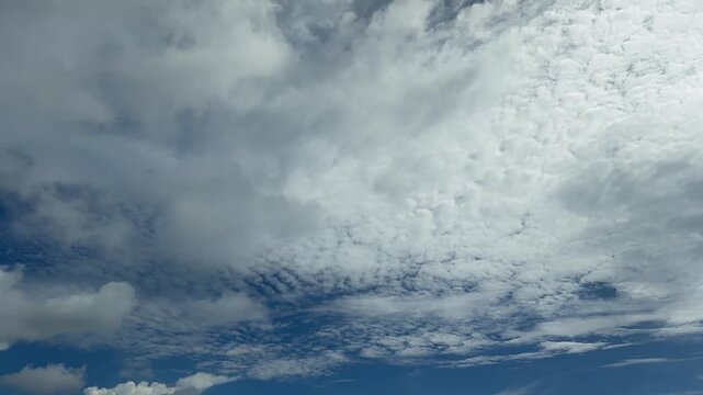 Time-lapse. A mesmerizing and unique time-lapse capture of dynamic layered sky movements, featuring swift, dense cumulus clouds shifting gracefully against patches of deep blue atmosphere. The natural