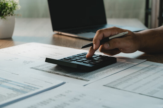 Close-up of hands using calculator over financial reports and spreadsheets with pen, showing financial data analysis, calculation and business number review.