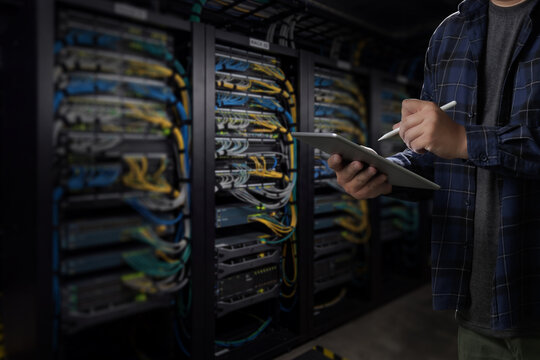 man engineer it support using tablet and stylus beside server racks in a data center, supporting network monitoring, IT infrastructure review and technical support workflow.