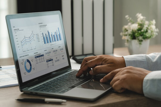 Businessman using laptop with financial dashboard and charts for data analysis, performance review and business reporting in office.