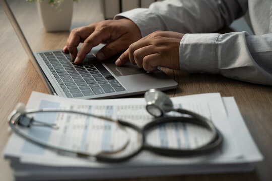 Close-up of hands typing on laptop beside stethoscope and medical paperwork, showing medical billing workflow, claim data review and healthcare administration.