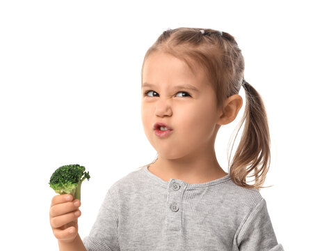 Healthy eating habits and picky eater concept, little girl making a disgusted face while holding a piece of fresh green broccoli isolated