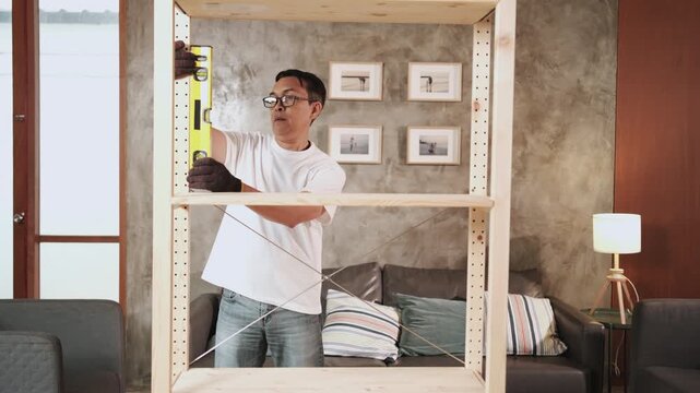 Asian mature man self-assembling furniture with DIY tools, checking endurance and accuracy with spirit&nbsp;level, home improvement, craft making, hobby wooden workshop, expert handyman, active lifestyle.