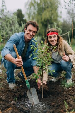 Happy couple planting a young tree together in garden, concept of new life and ecology