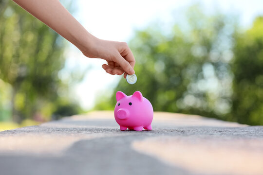 Financial savings and investment, person putting coin into pink piggy bank for future wealth planning and personal budget management in outdoor setting