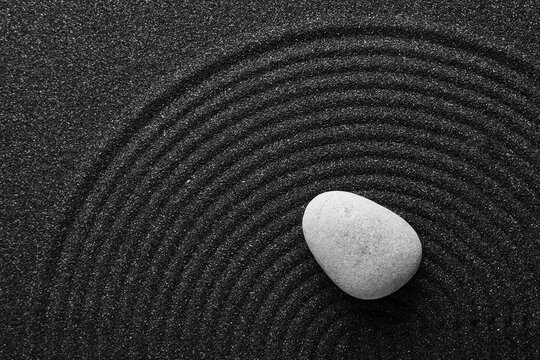 Mindfulness and zen meditation, smooth stone on raked black sand with circular patterns for stress relief and spiritual balance in a peaceful garden