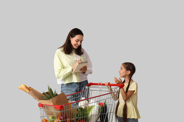 Family grocery shopping and budget planning, mother and daughter with shopping cart and list of food items on a plain light gray background © Pixel-Shot