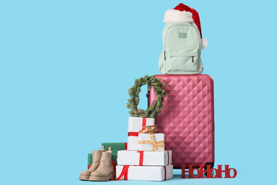 Holiday travel and winter vacation, luggage with christmas gifts and santa hat for seasonal trip planning on a blue background