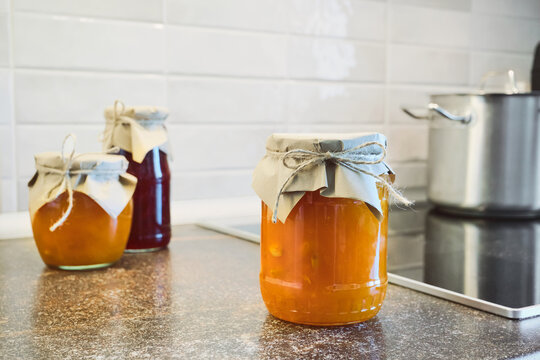 Preserving sweet homemade fruit jam and marmalade in glass jars on kitchen counter