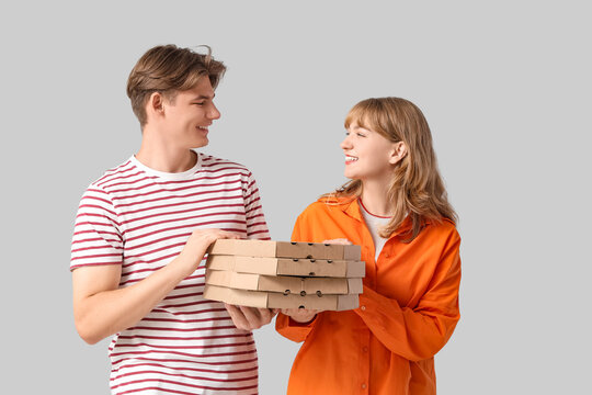 Food delivery and social gathering, happy young couple holding a stack of pizza boxes for a casual party or dinner at home on a light gray background