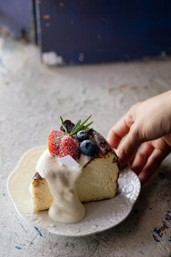Hand Placing Plate of Basque Burnt Cheesecake Topped with Cream and Fresh Berries.