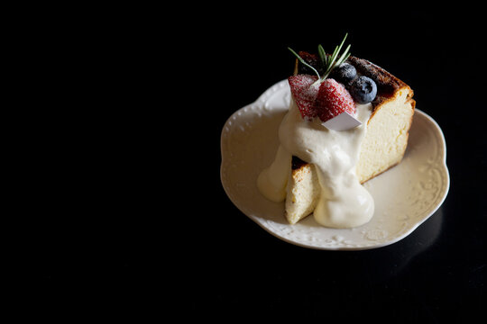 Slice of Basque Burnt Cheesecake Topped with Cream and Berries on Wooden Table