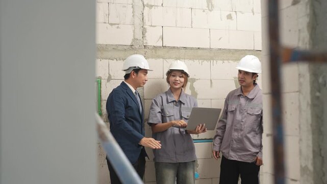 Structural engineer points toward building structure while architect and worker discuss construction progress during inspection at unfinished project site.