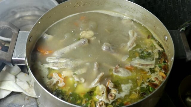 Chicken feet soup being cooked in a boiling pot in a home kitchen, showing a traditional homemade cooking activity.