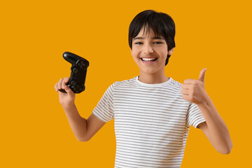 Gaming and entertainment, happy boy holding a video game controller and giving a thumbs up gesture on a solid yellow background © Pixel-Shot