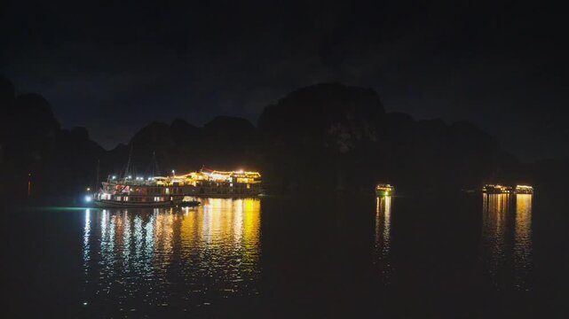 Night view of illuminated cruise ships anchored in Ha Long Bay, Vietnam, at dusk with dramatic sunset clouds and limestone karsts