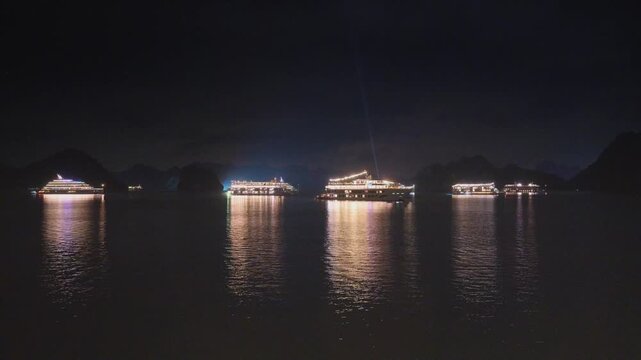 Night view of illuminated cruise ships anchored in Ha Long Bay, Vietnam, at dusk with dramatic sunset clouds and limestone karsts