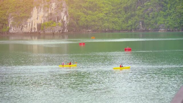 Tourists kayaking through an oyster pearl farm and lush green limestone mountain in Ha Long Bay, Vietnam