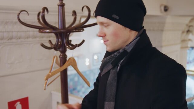 Close up of man adjusting his coat and backpack in well lit indoor setting with Christmas decorations. Man interacts casually moving slightly while carrying accessories background features