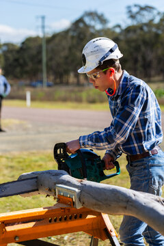 young man chainsawing up branch of gum tree for firewood