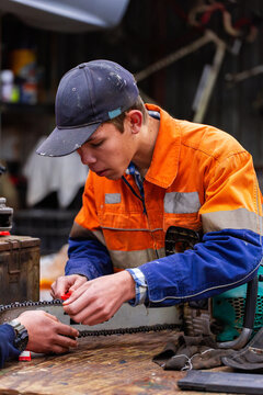 apprentice learning how to use file to sharpen chainsaw before work