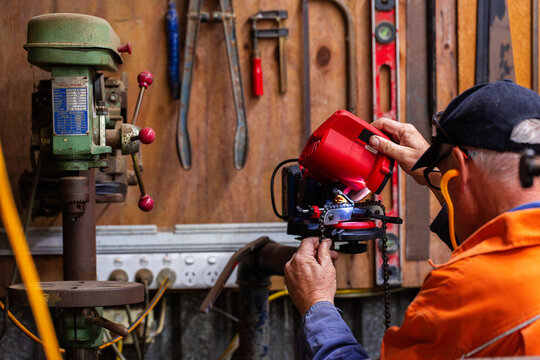 handyman in his fifties sharpening chainsaw teeth with electric sharpener tool in shed