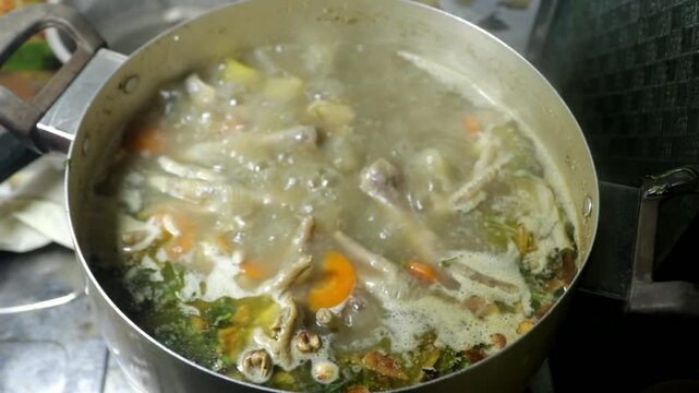 Chicken feet soup being cooked in a boiling pot in a home kitchen, showing a traditional homemade cooking activity.