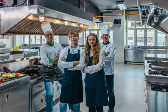 Team portrait of Asian chefs and teen culinary interns with arms crossed in a professional kitchen